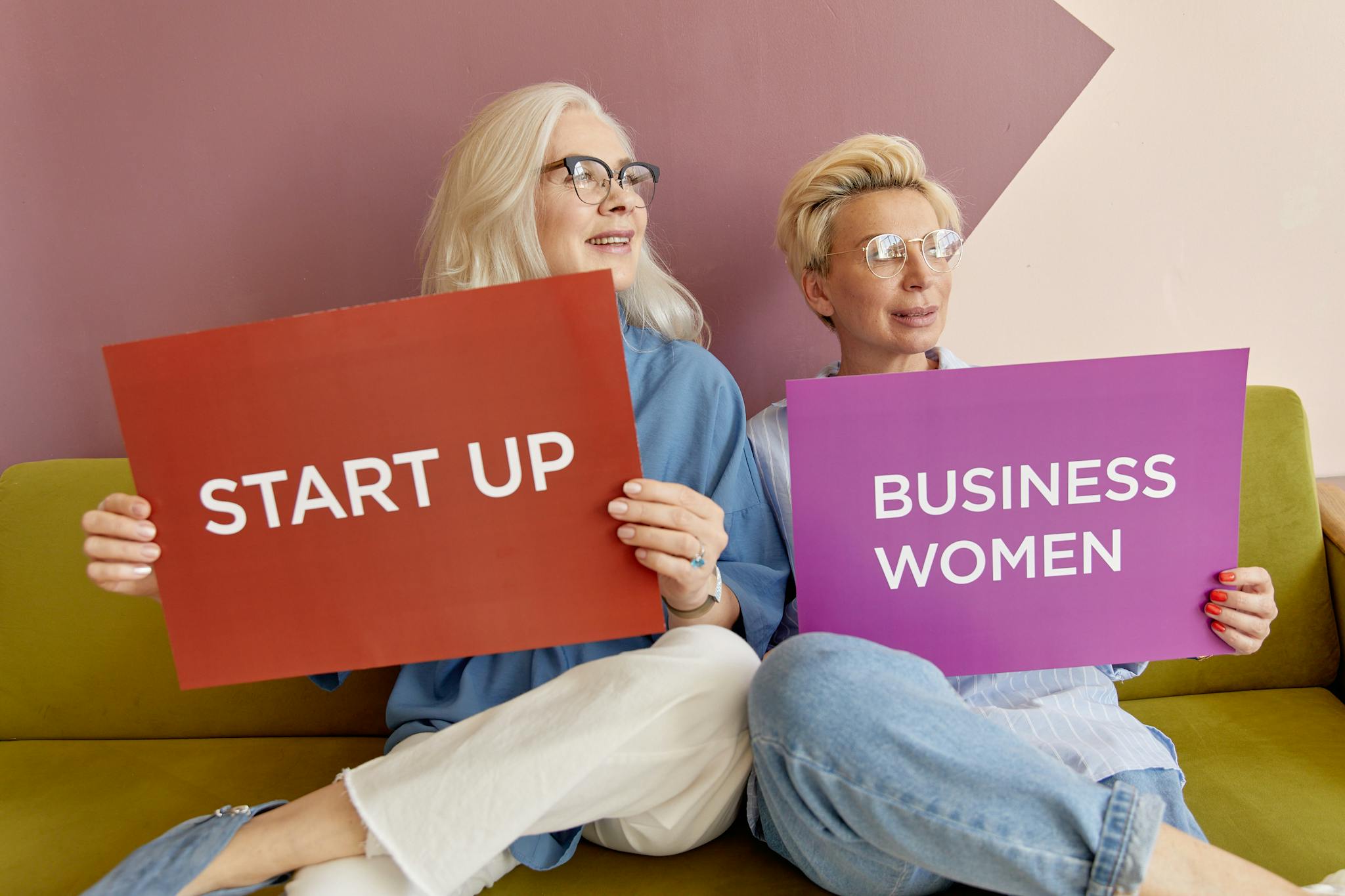 Two women on a sofa holding signs promoting startup and business women.