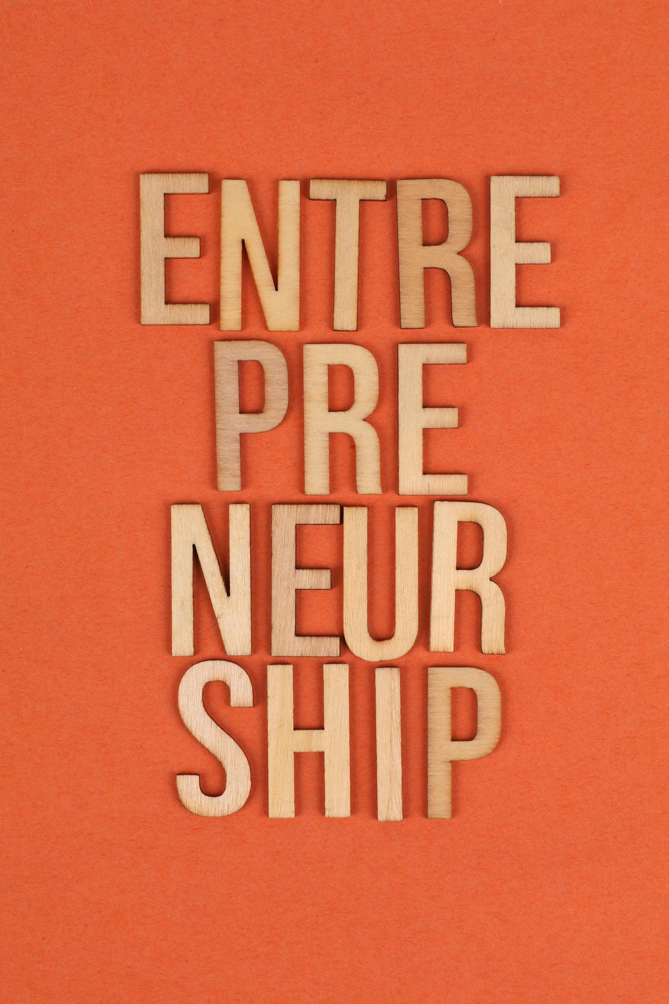 Wooden letters on orange background spelling 'ENTREPRENEURSHIP', symbolizing business aspirations.